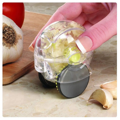 A clear roller garlic chopper with minced garlic inside, being held by a hand.